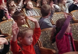 dzieci patrzą na scenę i trzymają ręce w górze