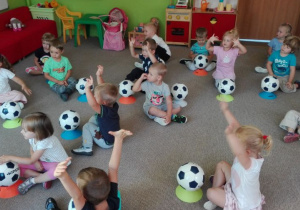 dzieci siedzą na dywanie z piłkami