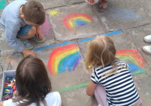 Dzieci rysują kredą na chodniku. 